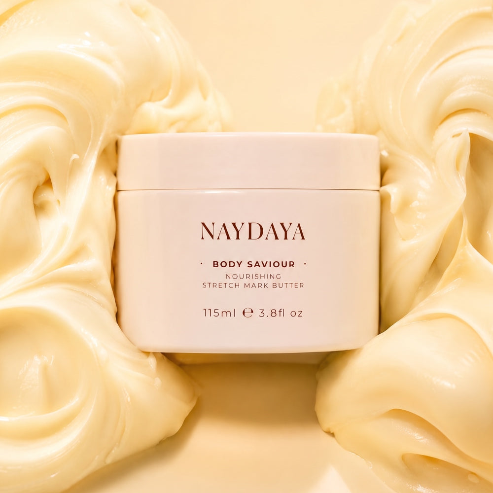 A cream-colored jar of NAYDAYA Body Saviour Stretch Mark Butter, centered against a background of glossy, swirled cream-colored product.