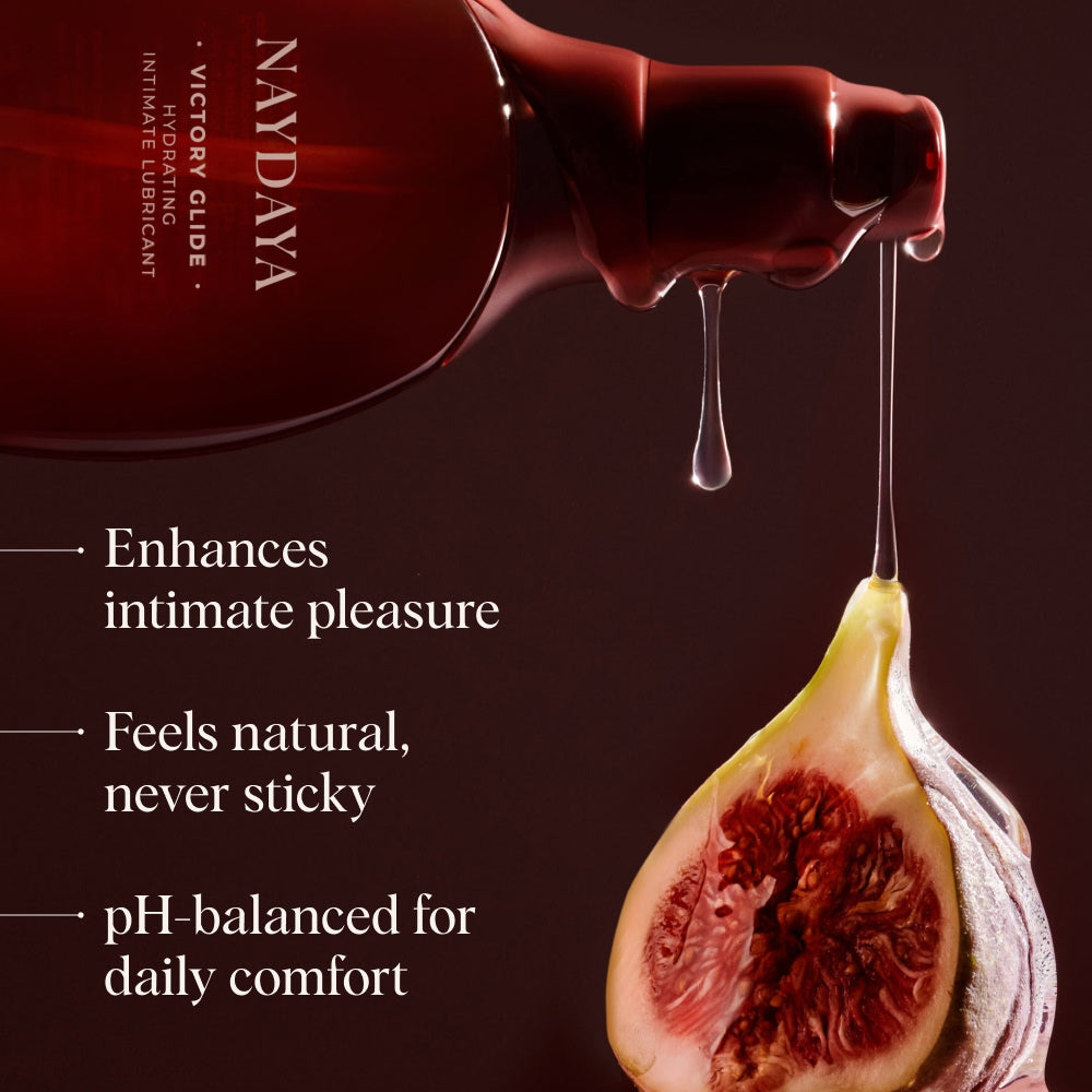 A dark red bottle of NAYDAYA Victory Glide intimate lubricant is shown with a fig cut in half, with liquid dripping from the bottle. Text on the left reads: 'Enhances intimate pleasure', 'Feels natural, never sticky', and 'pH-balanced for daily comfort'.
