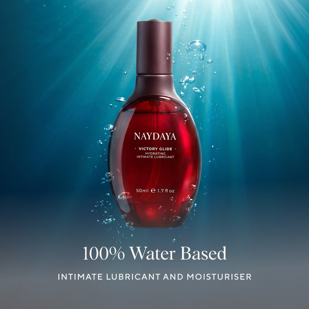 Naydaya Victory Glide water-based intimate lubricant bottle, shown in a glossy dark red color with a dark metallic cap, set against a blue underwater-themed background with light rays and bubbles. Text below reads '100% Water Based'.
